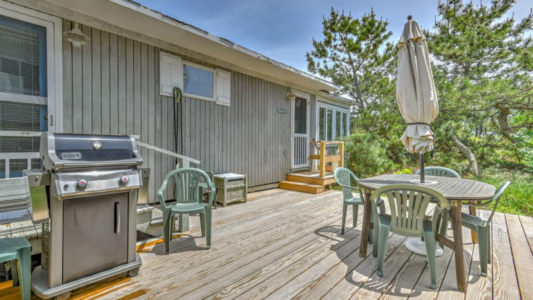 A wooden outdoor deck beside a house has a grill, seating, and a table.