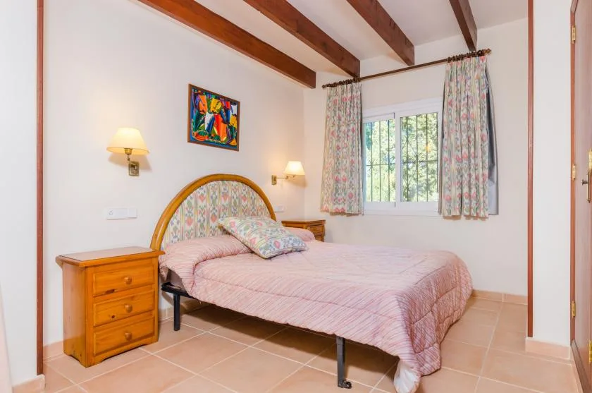 Un dormitorio con una cama, muebles de madera junto a ella y una ventana con cortinas.