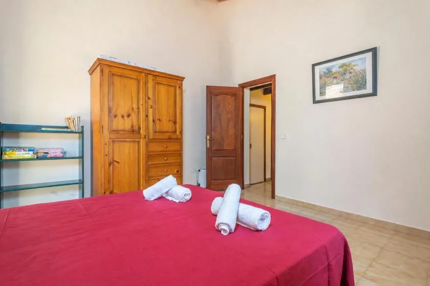 Un dormitorio con una cama cubierta de rojo, un armario de madera y una puerta abierta.