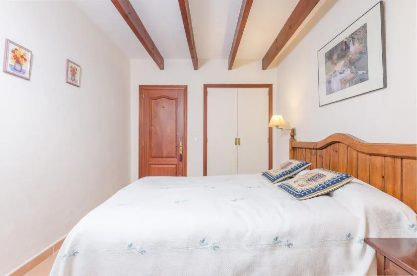Un dormitorio con una cama bien tendida y vigas de madera a la vista.