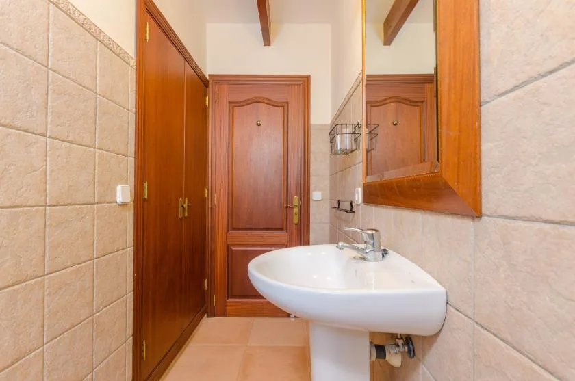 Un baño con lavabo de pedestal, paredes de azulejos y puertas de madera.