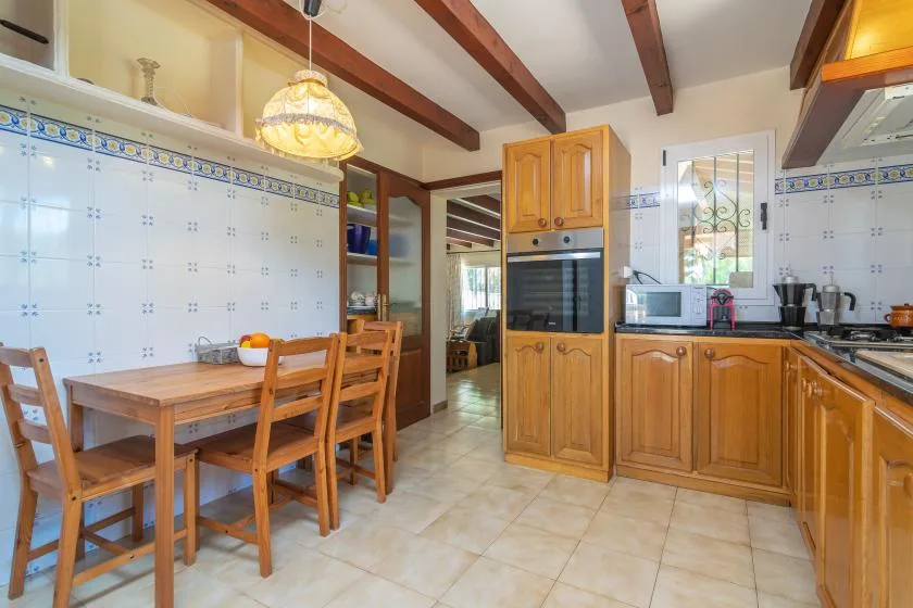 Una cocina alicatada con armarios de madera, una mesa de comedor y vigas expuestas.