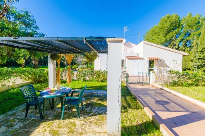 Un patio exterior con una zona de estar sombreada junto a un edificio blanco.