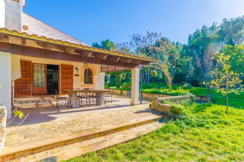 Un patio exterior cubierto con una mesa de comedor da a un jardín verde.