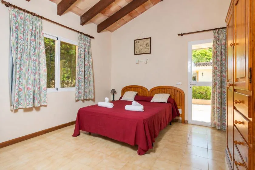 Un dormitorio con una cama doble cubierta con una colcha roja y ventanas con cortinas florales.