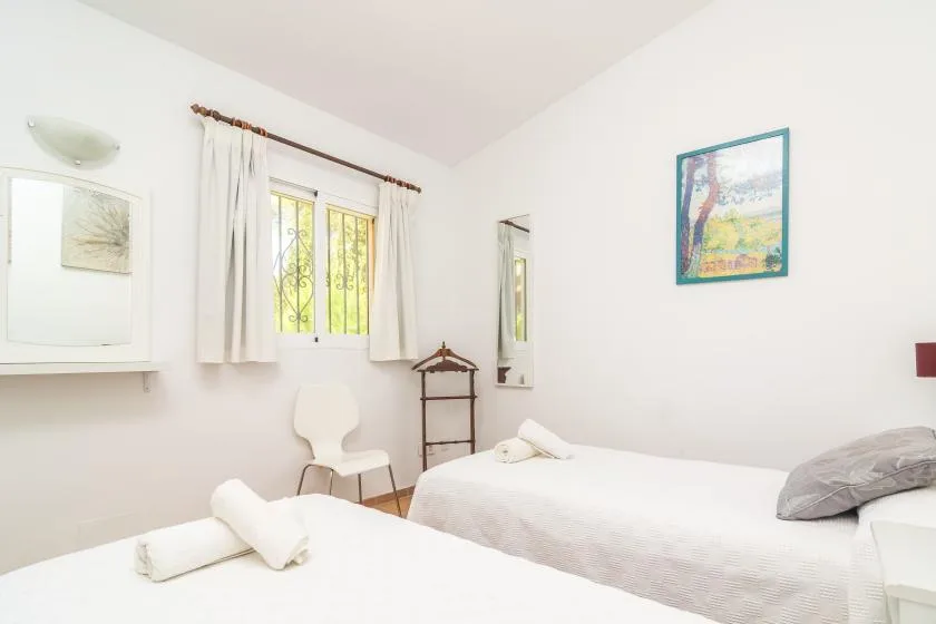 Un dormitorio luminoso con camas blancas, una ventana con cortinas y un cuadro enmarcado.
