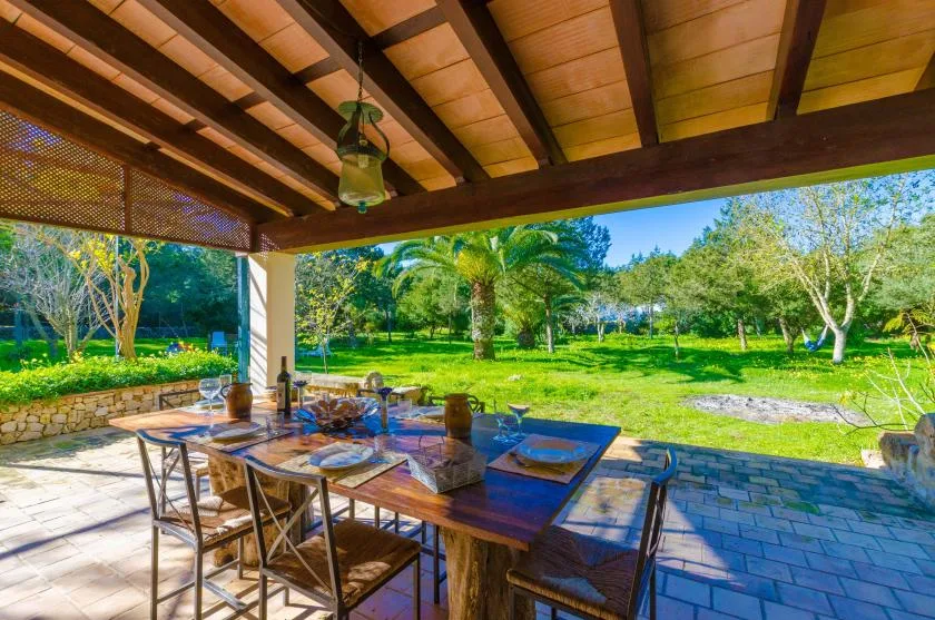 Una zona cubierta para comer al aire libre, con una mesa de madera frente a un jardín verde.