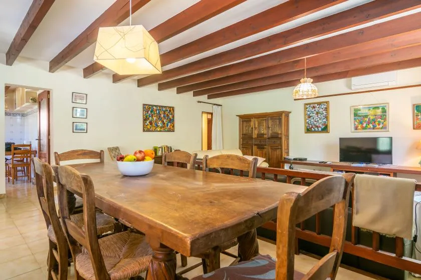 Un comedor con una mesa grande de madera, sillas y cuadros coloridos.
