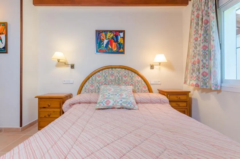 Un dormitorio con una cama doble, mesitas de noche y una obra colorida sobre el cabecero.