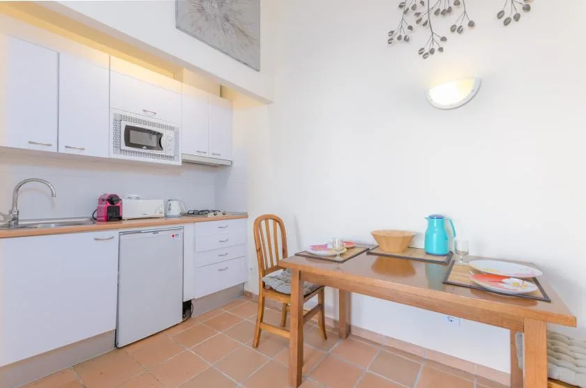 Una cocina y comedor luminosos con armarios blancos y una mesa de madera.
