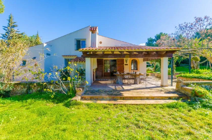 Una casa con patio cubierto, asientos al aire libre y jardín con césped.