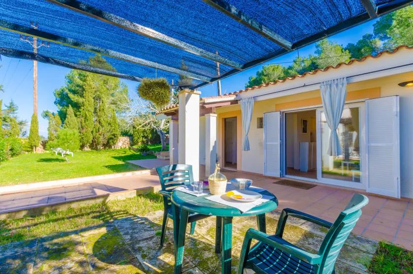 Un patio cubierto con asientos al aire libre da a un jardín y un edificio de tonos claros.