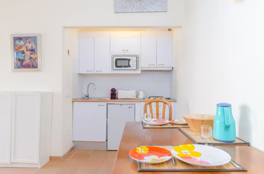 Una cocina compacta con armarios blancos, un fregadero y una mesa puesta con platos.