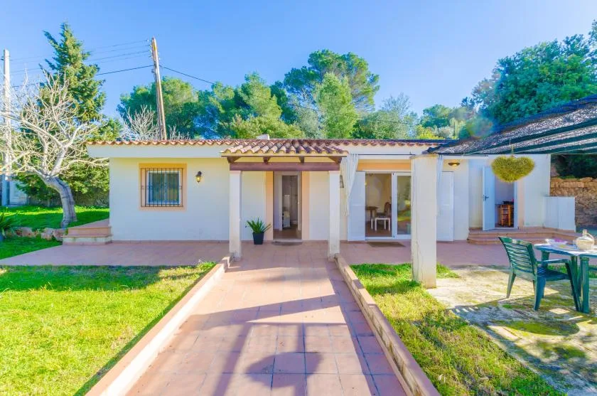 Una casa de una planta da a un patio pavimentado rodeado de césped verde.