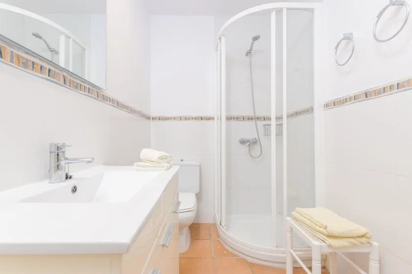 Un baño luminoso con lavabo, ducha y toallas dobladas.