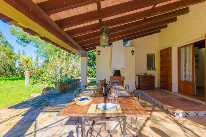Comedor exterior cubierto con una mesa larga junto a un jardín verde.