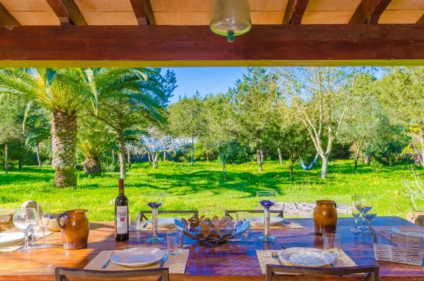 Una mesa de comedor al aire libre y cubierta da a un jardín verde y soleado.