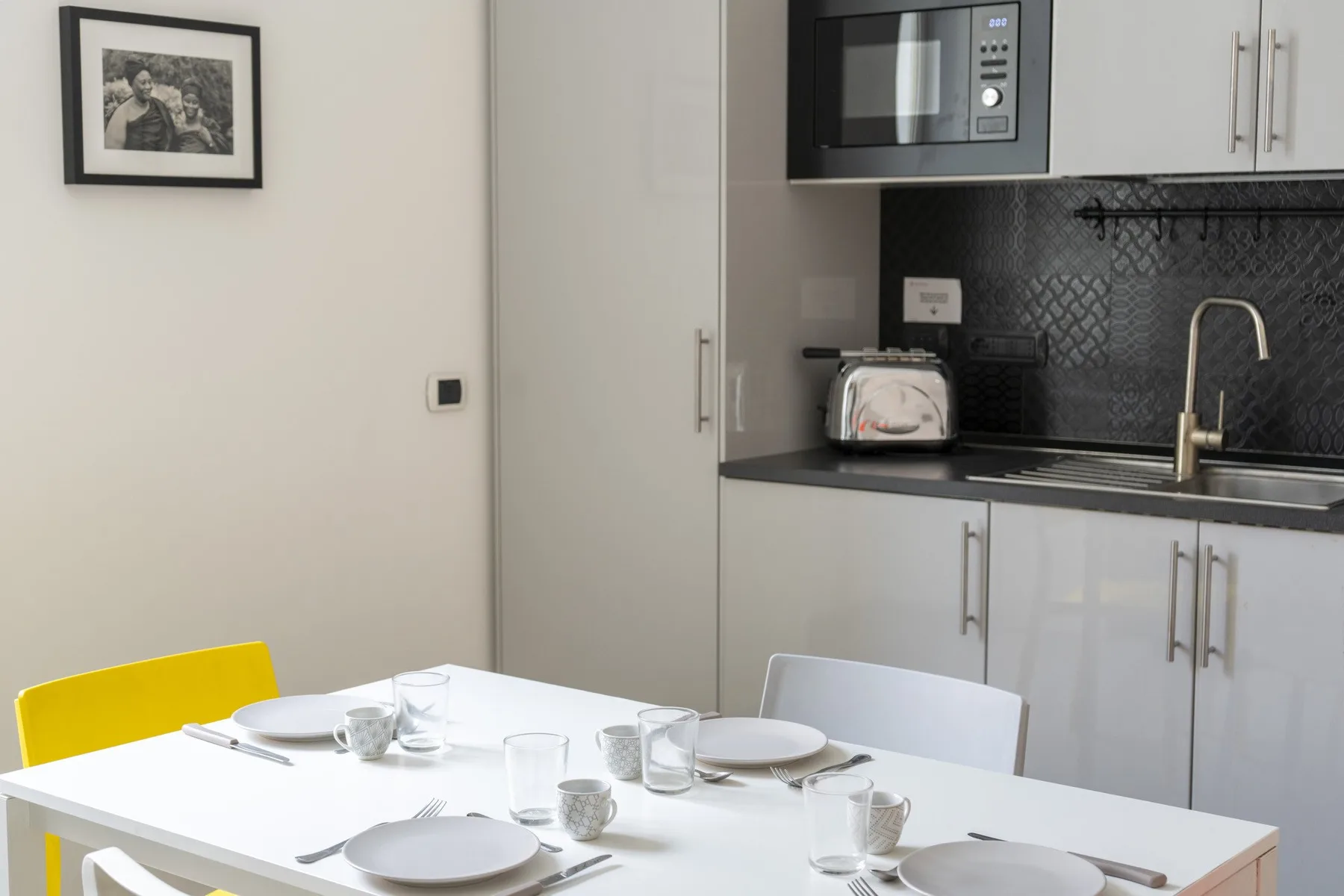 A dining table is set beside a compact kitchen with a dark backsplash.