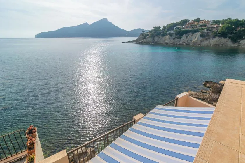 Una terraza junto al mar da a aguas tranquilas, con un toldo de rayas azules y blancas.