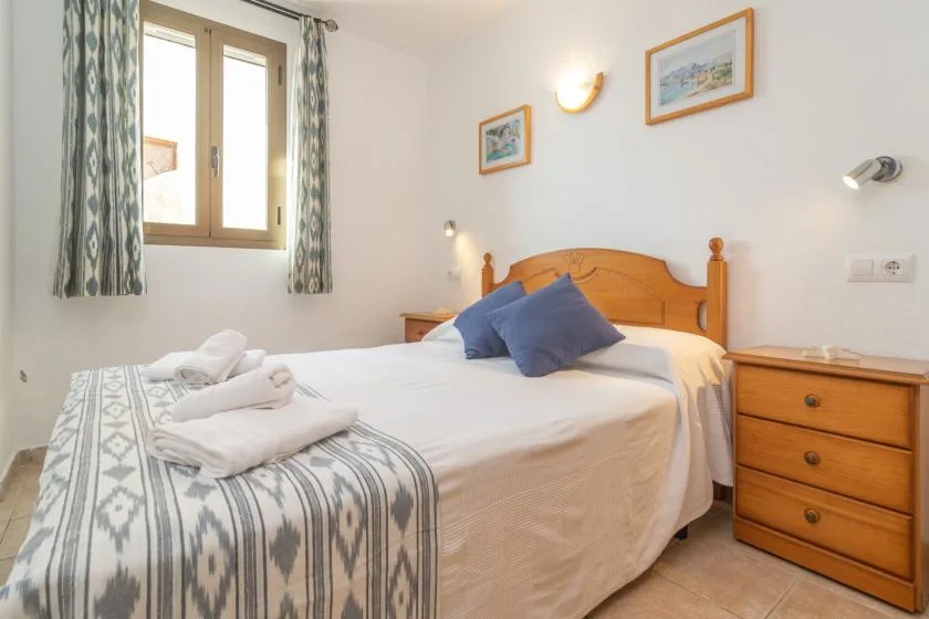 Un dormitorio con una cama de madera, almohadas azules y cortinas estampadas junto a la ventana.