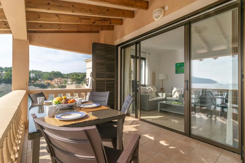 Una zona de comedor en una terraza cubierta se abre a una sala mediante puertas corredizas de vidrio.