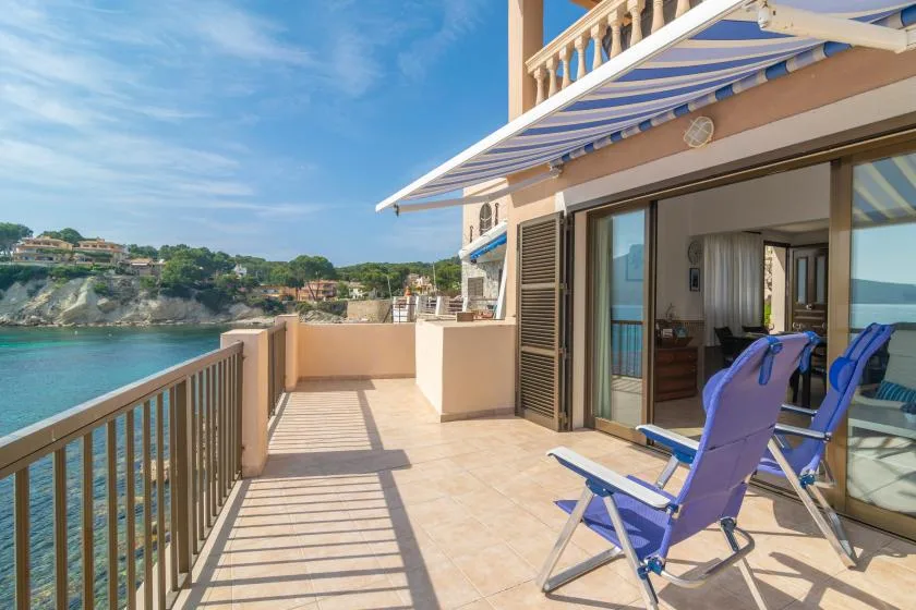 A sunny seaside terrace with blue lounge chairs and a view of the water.