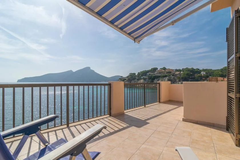 A tiled seaside terrace with lounge seating overlooks the water and distant hills.