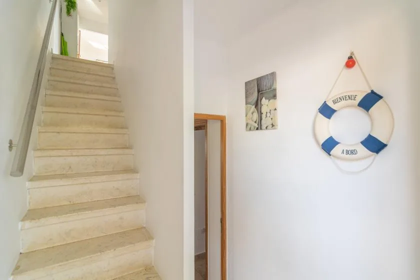 Un pasillo interior luminoso con una escalera y un salvavidas en la pared.