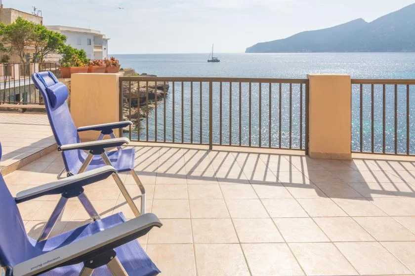 A seaside terrace overlooks the water, with outdoor seating beside a railing.