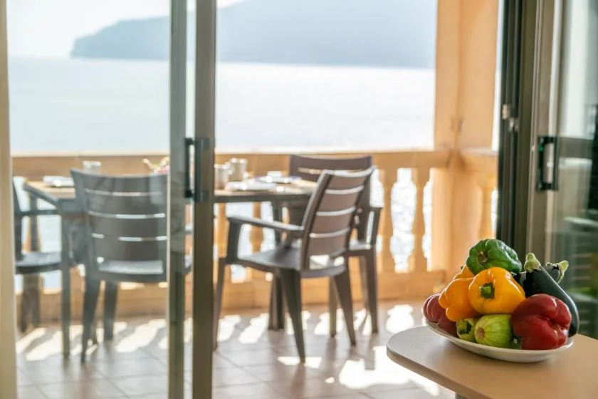 Un comedor da a una terraza junto al agua, con fruta sobre una mesa cercana.