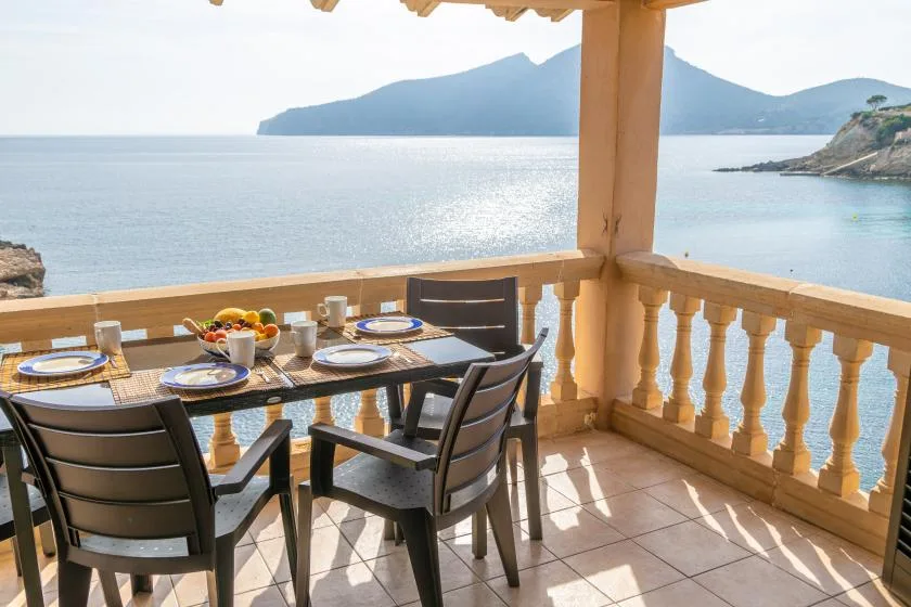 Una terraza junto al mar tiene una mesa puesta con vajilla y vistas al agua.