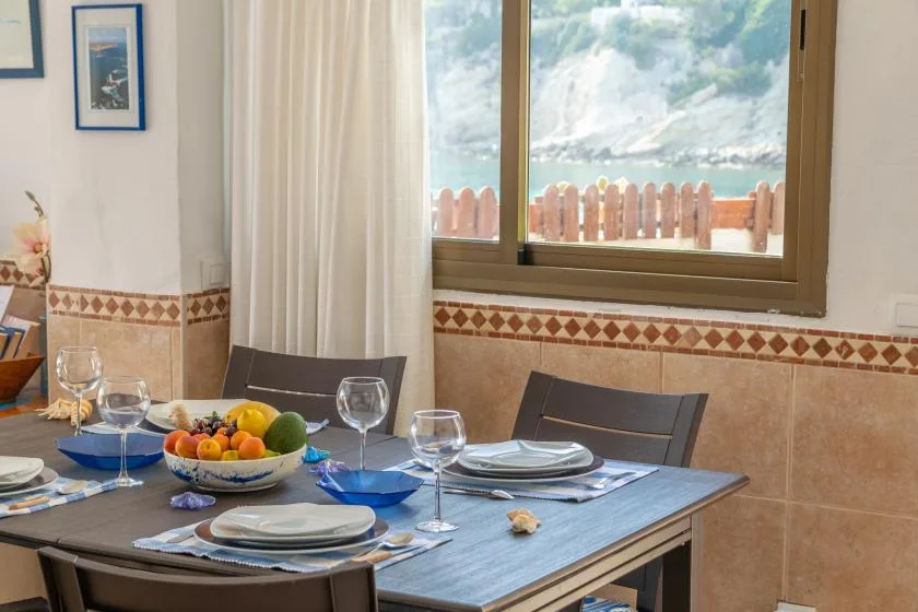 Una mesa de comedor está puesta con platos y fruta junto a una ventana grande.