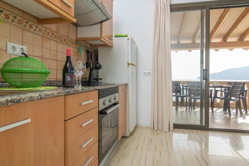 Una cocina con gabinetes de madera da a un patio cubierto con asientos al aire libre.