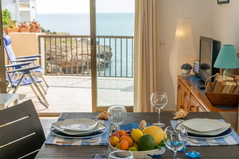 Una mesa preparada para comer da a un balcón y al mar.