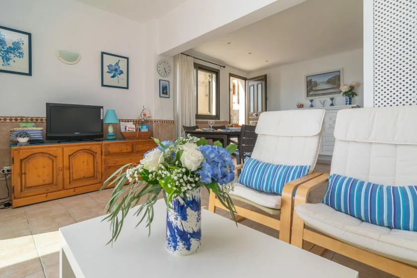 Una sala luminosa con asientos acolchados, un televisor y flores sobre la mesa.