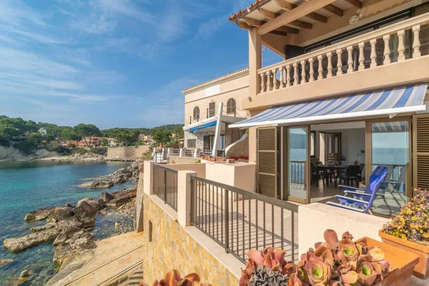 A seaside terrace overlooks the water, with outdoor seating beneath a striped awning.