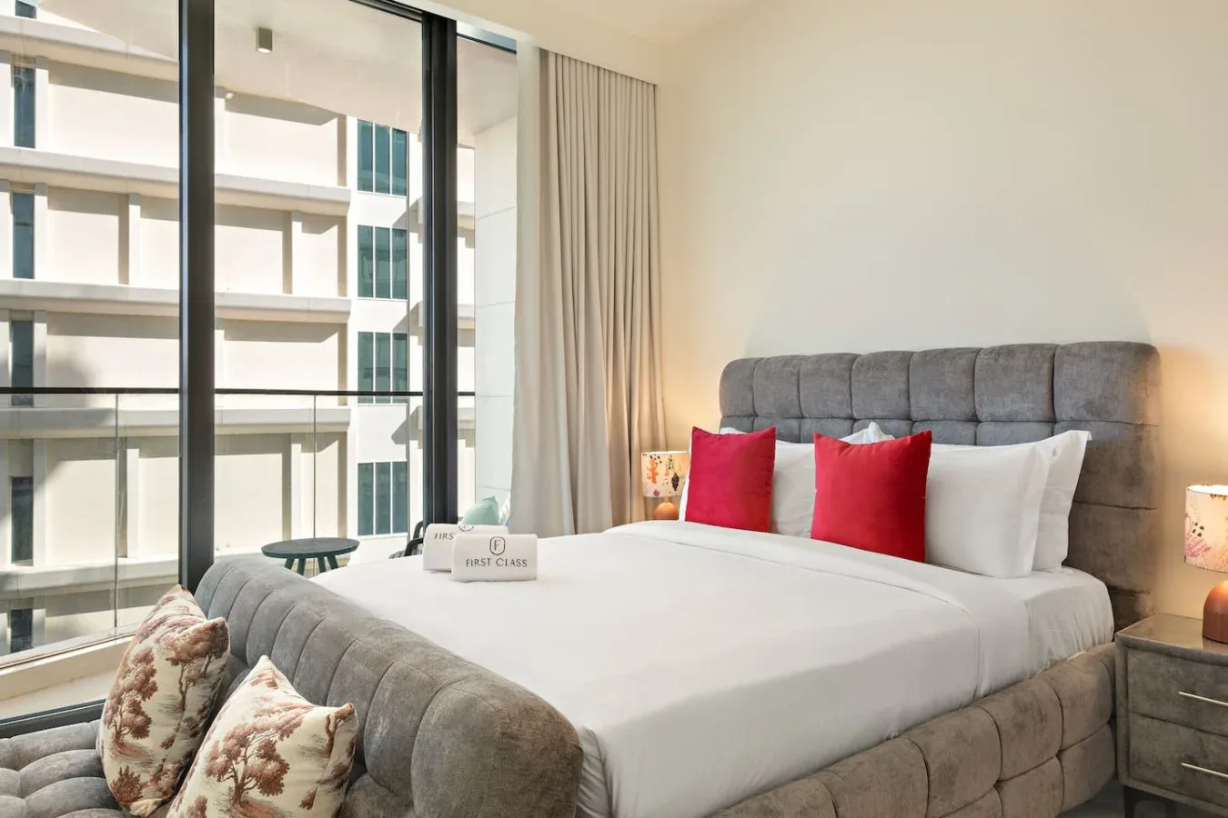 Un dormitorio con una cama grande, cabecera gris tapizada y cojines decorativos rojos.