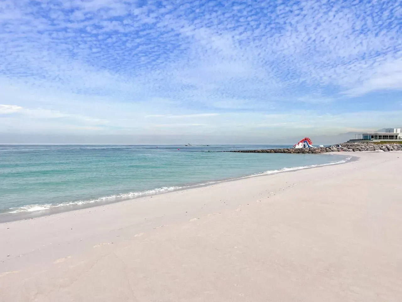 Una playa de arena se encuentra con aguas turquesas tranquilas bajo un cielo nublado.