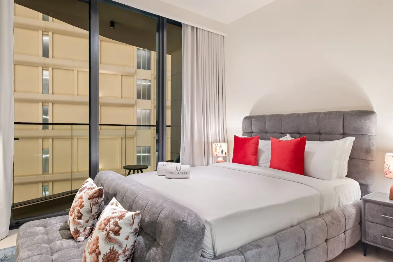 Un dormitorio con una cama grande, cojines rojos y ventanales de piso a techo.