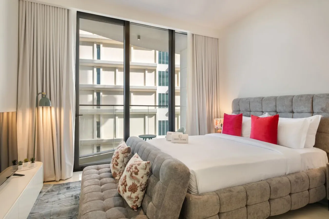 Un dormitorio con una cama grande, asientos grises y ventanales de piso a techo.