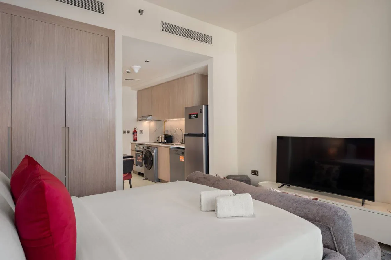 Un dormitorio con una cama, un televisor y una pequeña cocina al fondo.