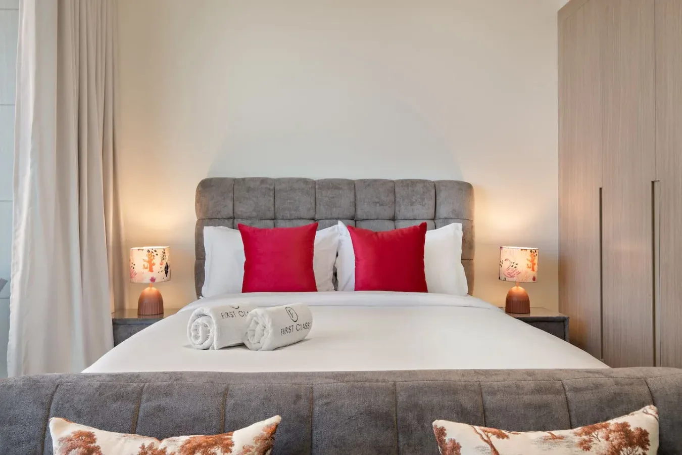 Un dormitorio con una cama tendida, cojines rojos y lámparas de mesita.