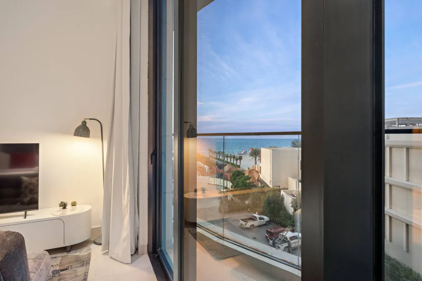 Una sala luminosa con un televisor junto a un gran ventanal con vistas al mar.