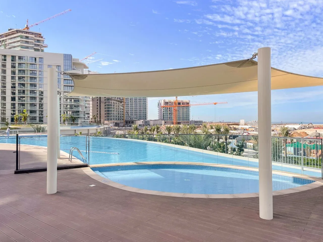 Una piscina al aire libre está bajo una gran cubierta de sombra, con edificios altos al fondo.