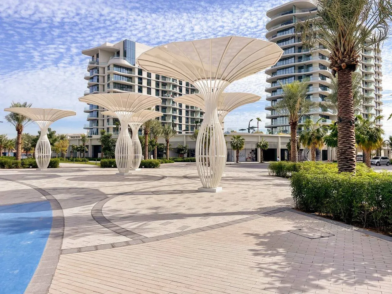 Una plaza exterior ajardinada con marquesinas escultóricas junto a edificios modernos.