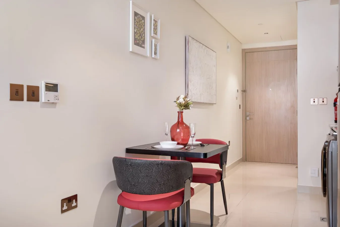 Un comedor con una mesa pequeña, asientos y un jarrón rojo.