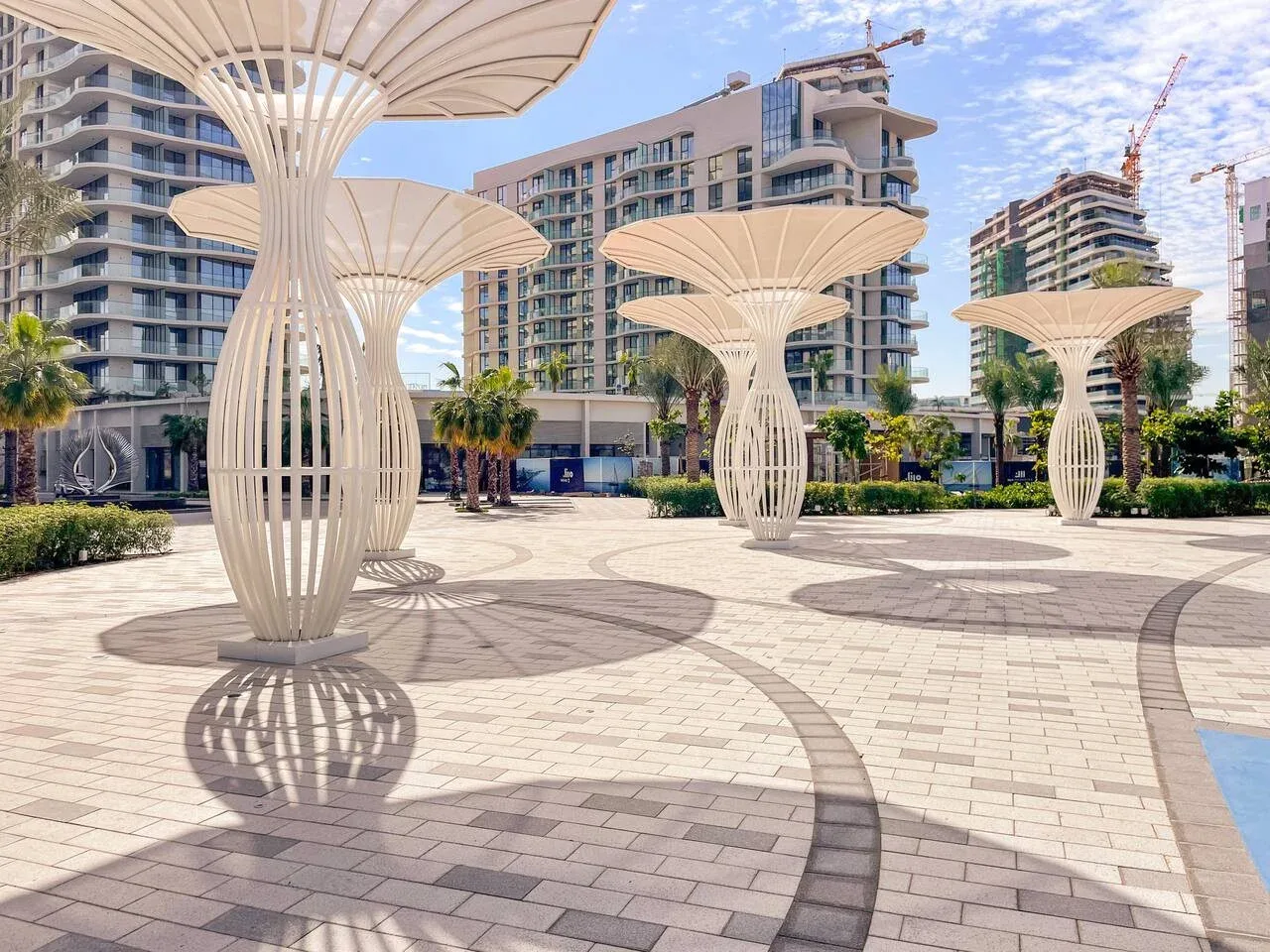 Una plaza exterior pavimentada cuenta con estructuras blancas de sombra y vegetación.
