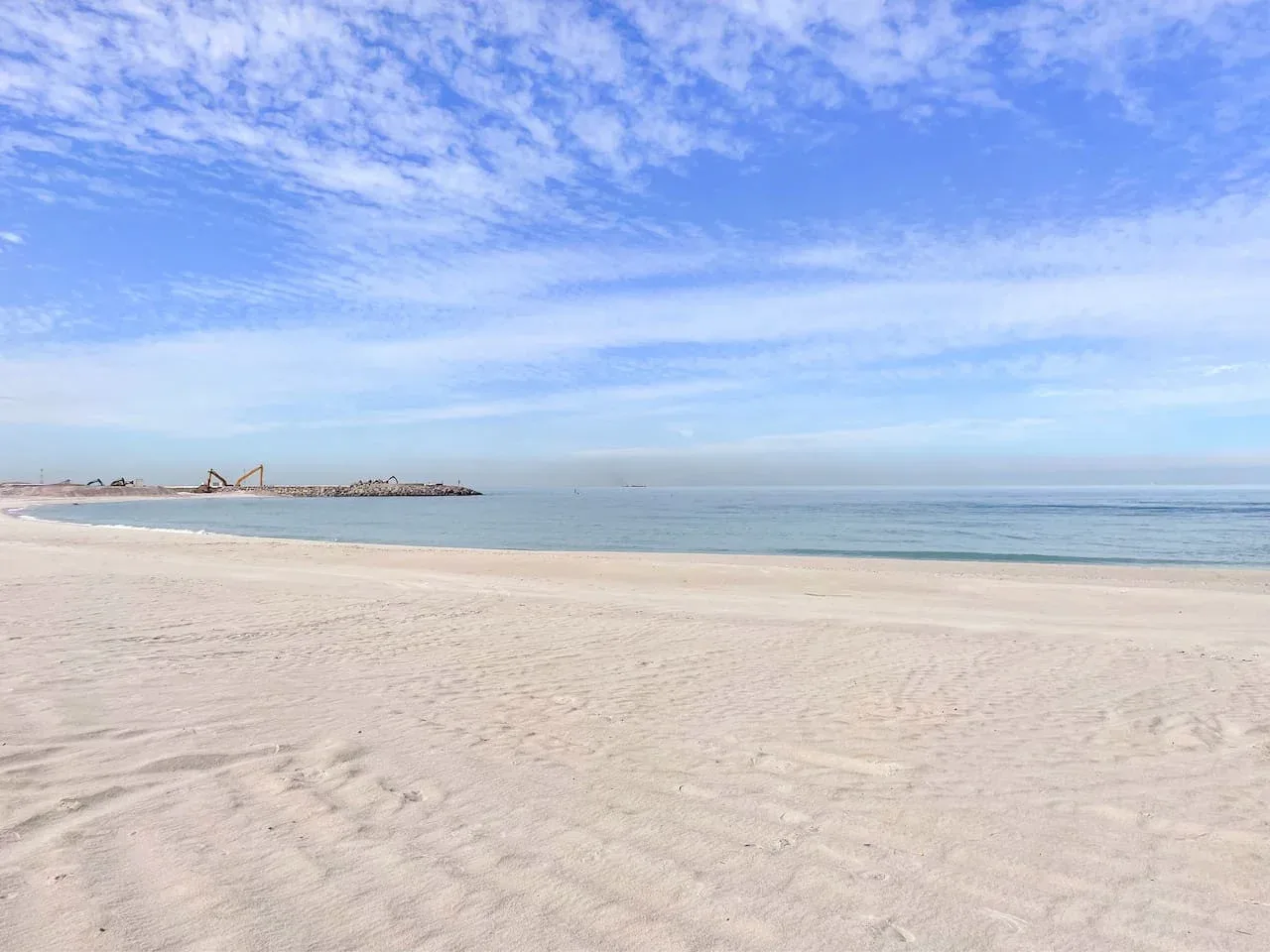 Una playa de arena se encuentra con aguas tranquilas bajo un cielo parcialmente nublado.