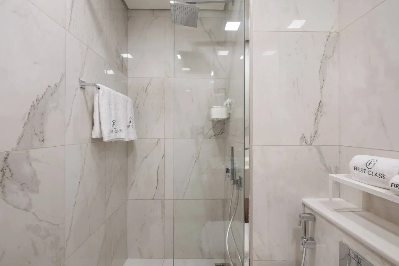Una ducha de baño con azulejos, paneles de vidrio, un toallero y una pequeña repisa.
