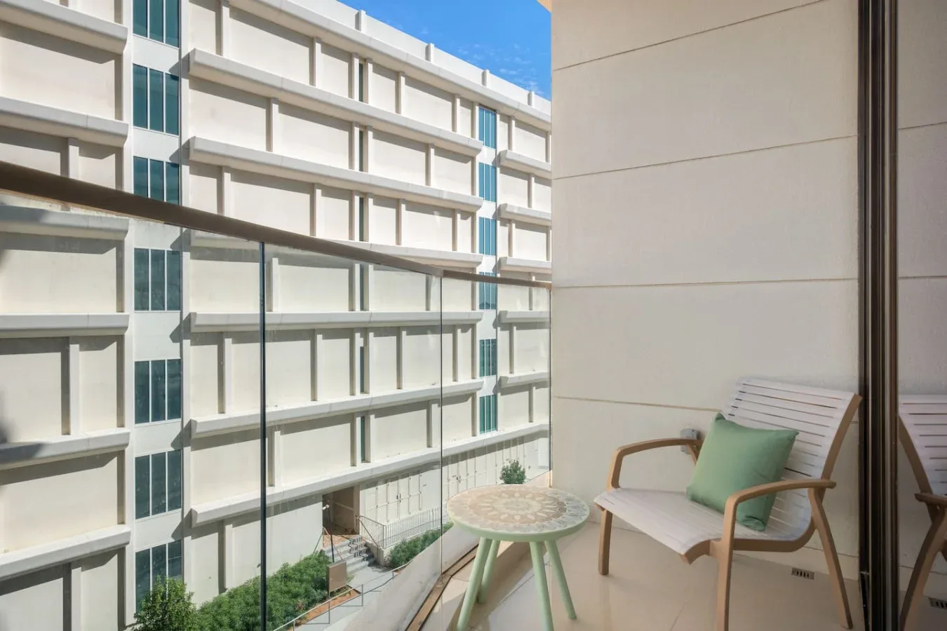 Una zona de estar en un balcón da a un edificio moderno, con una mesita junto al asiento.